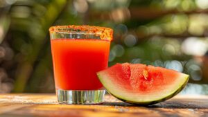 A vibrant pink Mexican Candy Shot in a glass with a chili-lime seasoning rim.