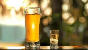 A Skittle Bomb Shot with a shot glass of Triple Sec dropped into a larger glass of a yellow energy drink.