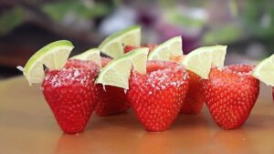 A tray of Strawberry Margarita Jello Shots in plastic cups with salt rims and lime garnishes.